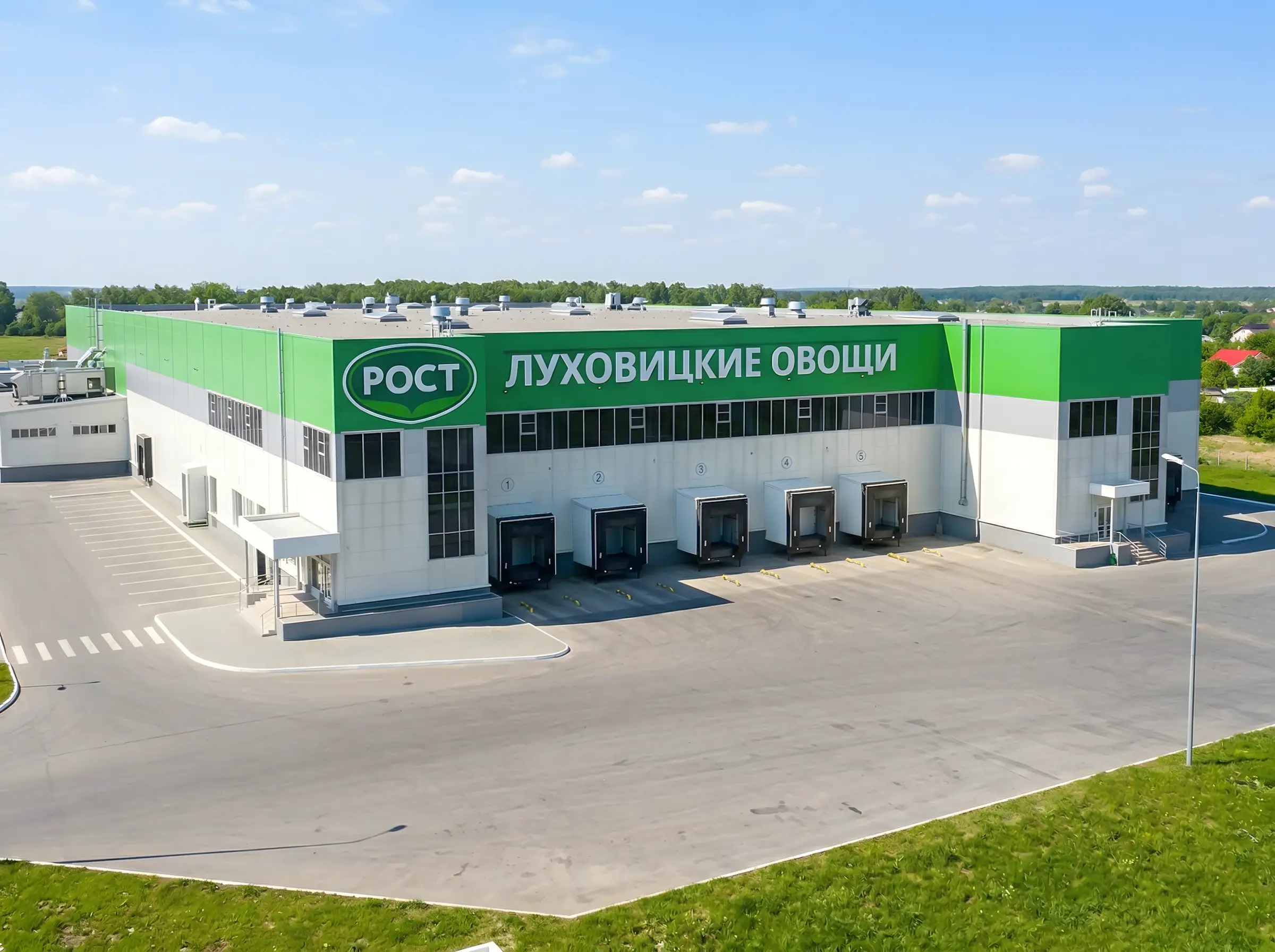 Современное здание логистического центра «Луховицкие овощи» с зелёной вывеской РОСТ и зонами для погрузки грузовиков, асфальтированная площадка и зелёные насаждения вокруг